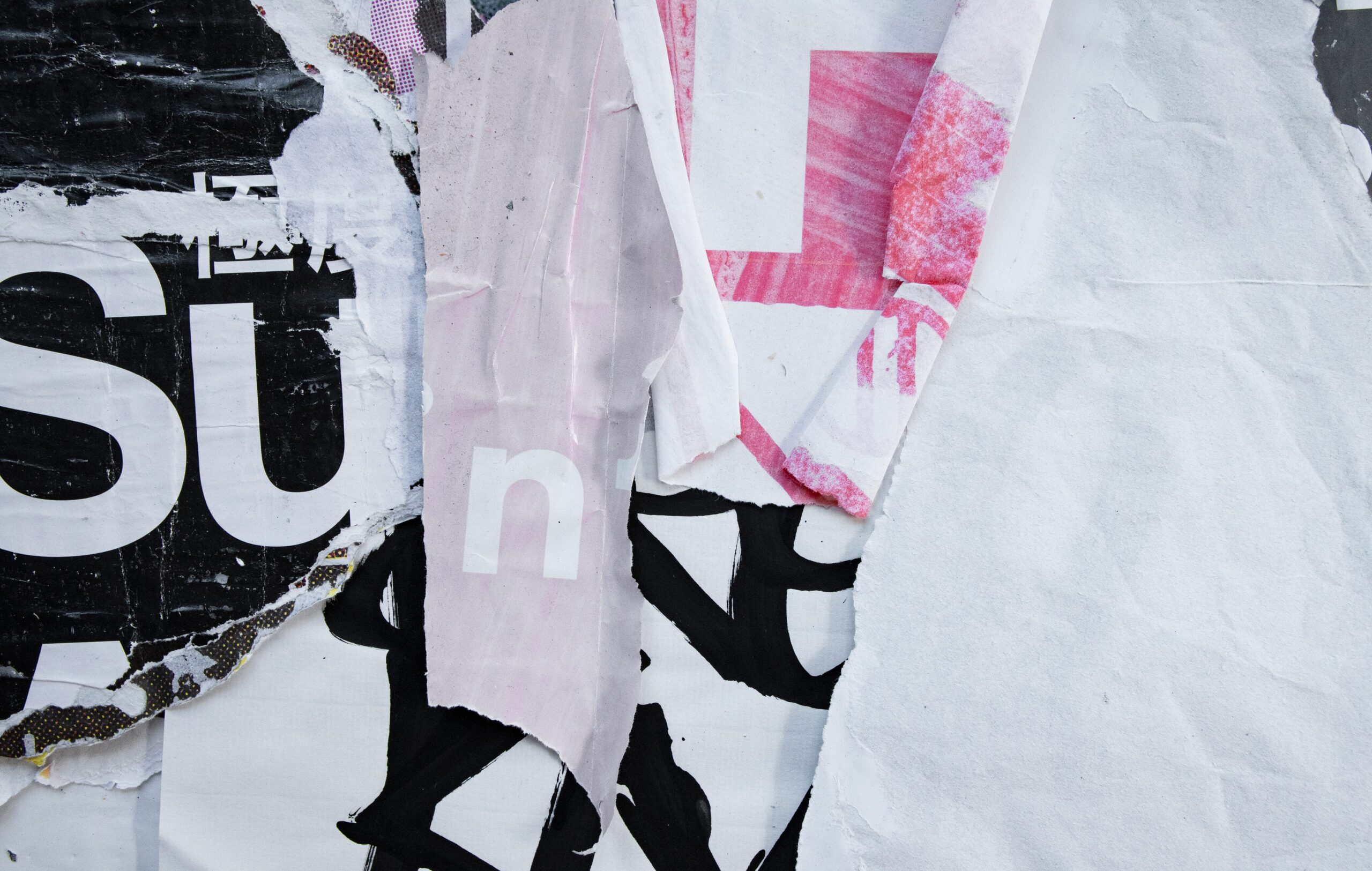 Close-up of torn and layered street posters with bold typography and abstract textures in black, white, and pink representing trending words that shaped 2024